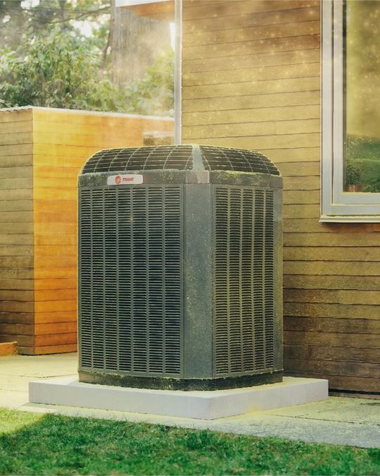 A Trane condenser beside a home in late-day light